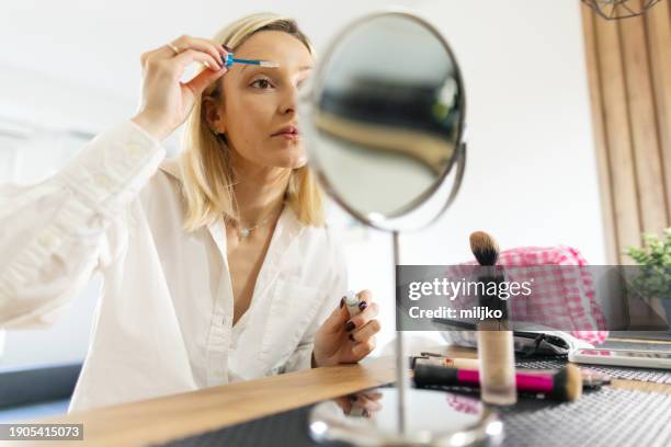 a beautiful young woman applying make up in her living room - correction fluid stock pictures, royalty-free photos & images