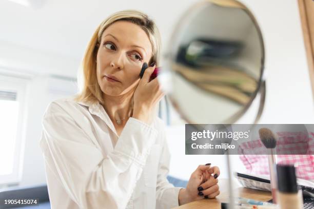 a beautiful young woman applying make up in her living room - tipp ex stockfoto's en -beelden