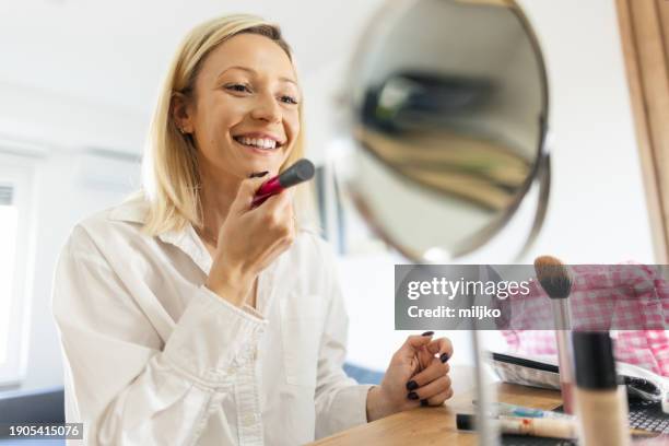 a beautiful young woman applying make up in her living room - correction fluid stock pictures, royalty-free photos & images