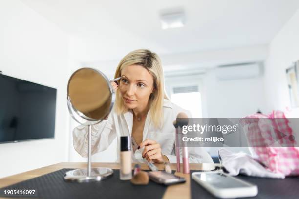 a beautiful young woman applying make up in her living room - correction fluid stockfoto's en -beelden