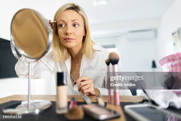 a beautiful young woman applying make up in her living room - eyebrow pencil stockfoto's en -beelden