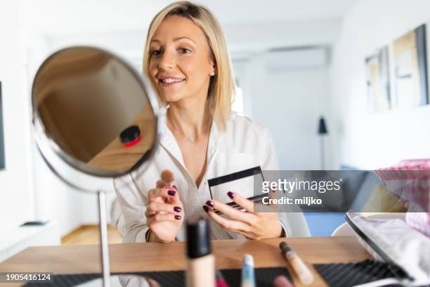a beautiful young woman applying make up in her living room - tipp ex stockfoto's en -beelden