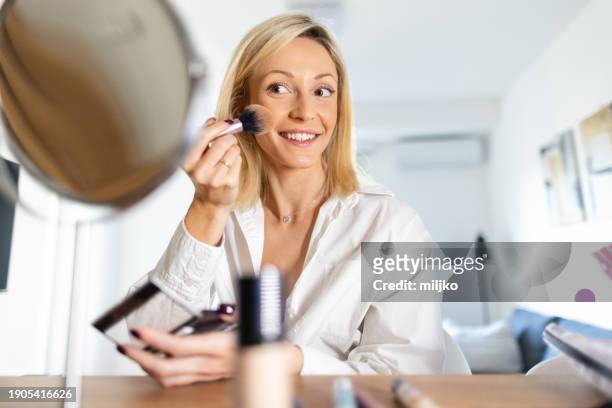 a beautiful young woman applying make up in her living room - correction fluid stockfoto's en -beelden