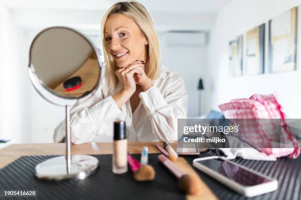 a beautiful young woman applying make up in her living room - correction fluid stock pictures, royalty-free photos & images