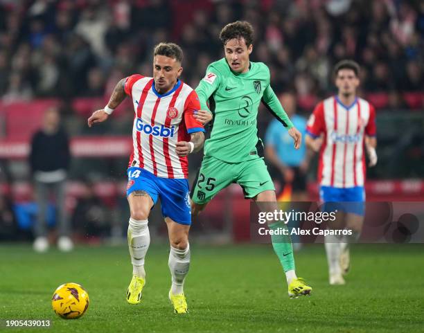 Aleix Garcia of Girona FC runs with the ball under pressure from Rodrigo Riquelme of Atletico Madrid during the LaLiga EA Sports match between Girona...