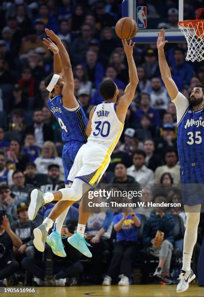Stephen Curry of the Golden State Warriors shoots over Jalen Suggs and Goga Bitadze of the Orlando Magic during the first quarter of an NBA...
