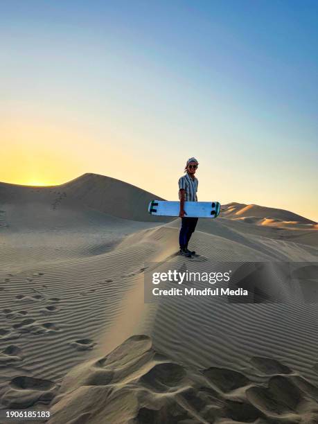 portrait of young man standing on sand dunes holding sandsurfing board in huacachina, ica, peru - footsteps on a boardwalk bildbanksfoton och bilder