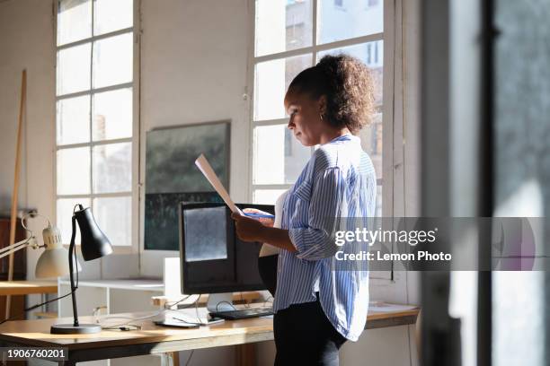 plan moyen d’une femme enceinte d’ascendance africaine examinant des documents dans un bureau moderne de coworking - dascendance européenne photos et images de collection