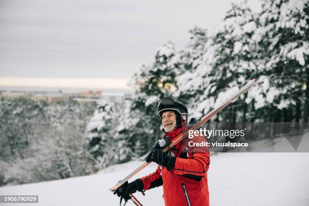 senior man walking on a snowy slope, with skis on shoulder - estonia forest stock pictures, royalty-free photos & images