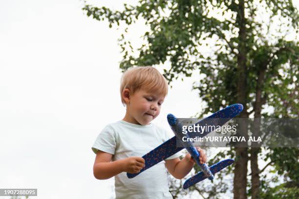 a happy and cheerful child boy in red shorts in a village or in a country house in the backyard on a sunny day, launches a blue children's airplane in the summer. - launching event stock pictures, royalty-free photos & images