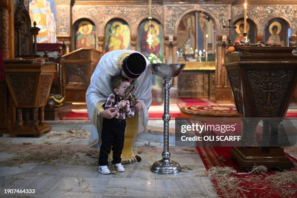 Serbian Orthodox Christian priest, Father Nenad Popovic invites a young worshipper Maksim, aged 2, to kiss his cross and receive bread following a...