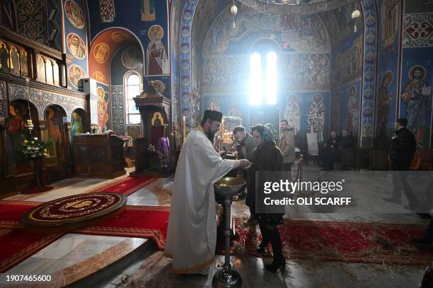 Serbian Orthodox Christian priest, Father Nenad Popovic invites worshippers to kiss his cross and receive bread following a service of the Nativity...
