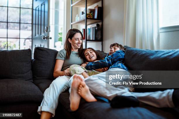 playful kids on the couch with their mom - familie stockfoto's en -beelden