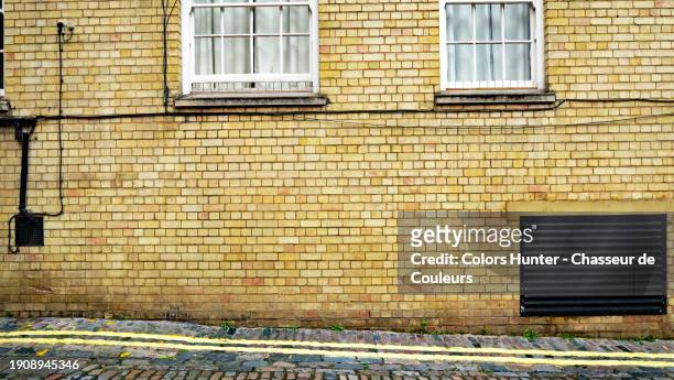 a yellow brick facade with windows, ventilation grid and electrical cables in london, england, united kingdom. paved sidewalk and street. no people. - lawn aeration stock pictures, royalty-free photos & images