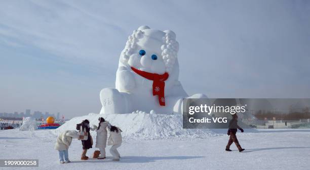 People take photos of a 20-meter-tall curly-haired snow sculpture wearing a red scarf near the Songhua River on January 4, 2024 in Harbin,...