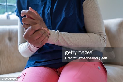 black woman wearing medical scrubs wrings hands together showing emotional stress or physical pain