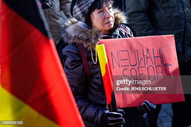 Protester holds a German flag and a poster claiming for immediate new elections as she takes part in a demonstration against the federal government's...