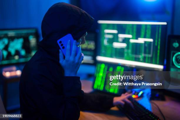 anonymous computer hacker in white mask and hoodie. obscured dark face using laptop computer for cyber attack and calling on cellphone, - scammer trickbetrüger stock-fotos und bilder