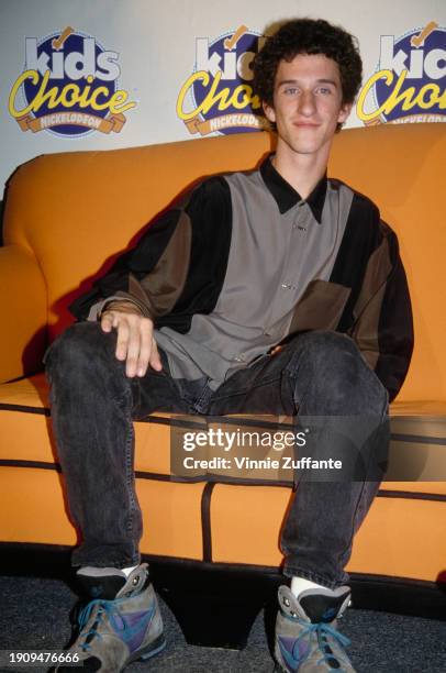 American actor and comedian Dustin Diamond, wearing a grey, black and olive green shirt, sitting on an orange sofa in the press room of the 1992...