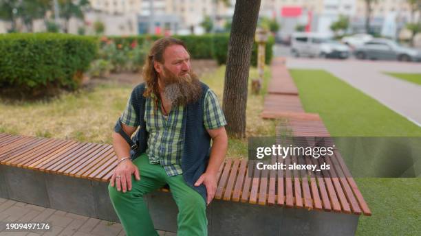 long-bearded elderly man sitting alone on a park bench and looking away - ginger bush stock pictures, royalty-free photos & images