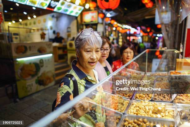 three mature asian women, about 70 years old, are visiting the night market in jiufen, taipei, which is a popular tourist attraction. they are choosing braised food and queuing up to buy it. - taiwanese ethnicity stockfoto's en -beelden