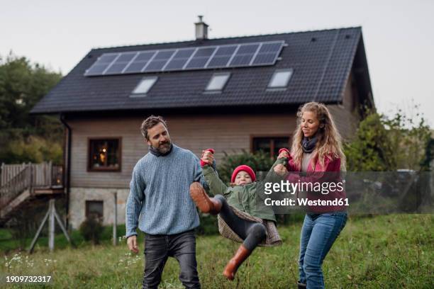 happy parents holding hands and playing with daughter in front of house - fuel and power generation stock-fotos und bilder