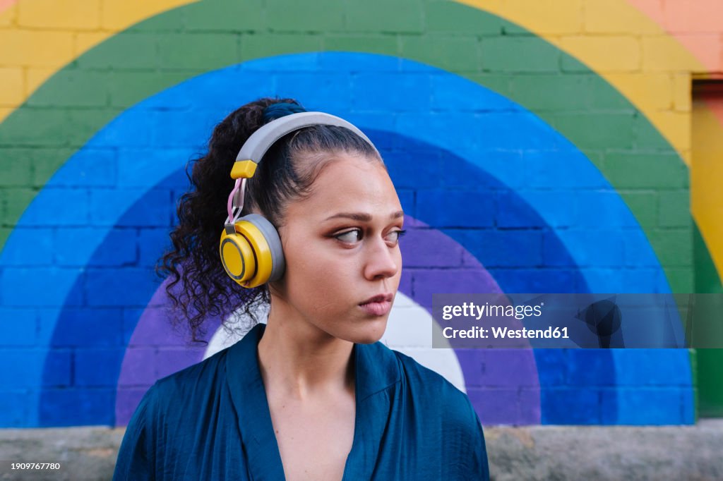 Woman wearing wireless headphones in front of rainbow wall