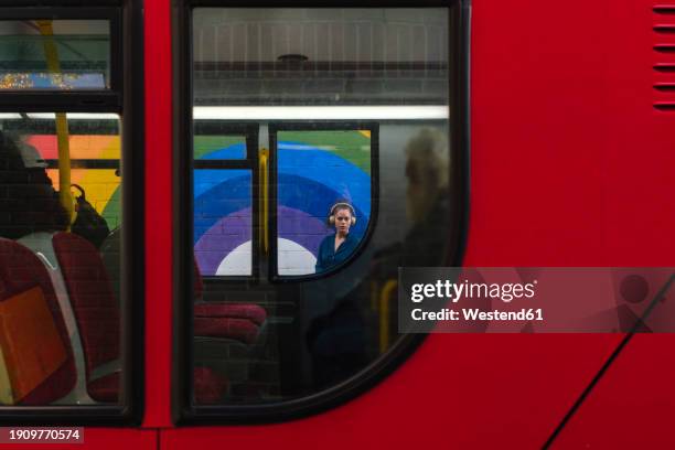 woman wearing wireless headphones seen through bus window - out bus window stock pictures, royalty-free photos & images
