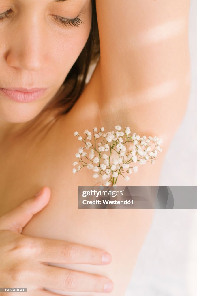Woman with flowers on armpit against white background