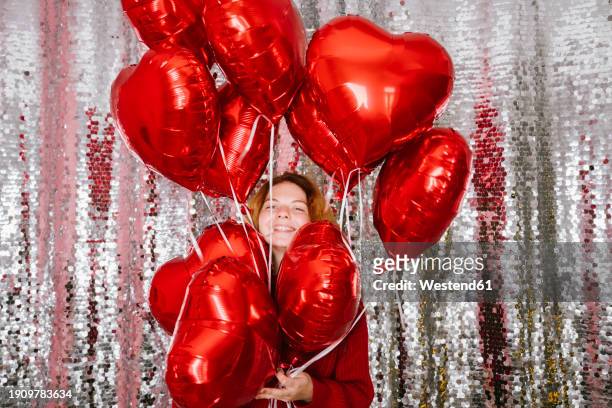 happy woman holding heart shaped balloons in front of sequin curtain - silver balloon imagens e fotografias de stock