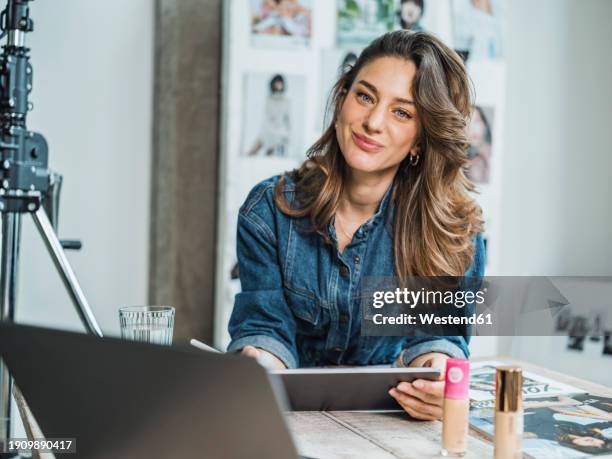 smiling influencer holding tablet pc at desk in studio - osteuropäischer abstammung stock-fotos und bilder