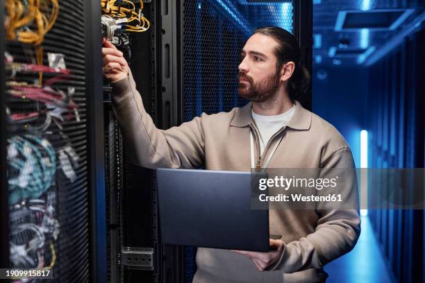 it professional holding laptop and examining cables in server room - server room stock pictures, royalty-free photos & images