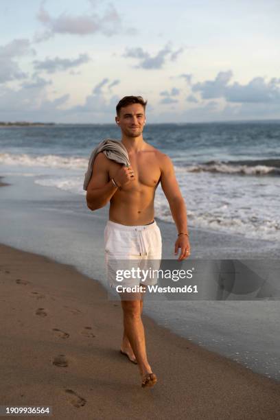 smiling shirtless man walking at beach - indonesia beach stock pictures, royalty-free photos & images