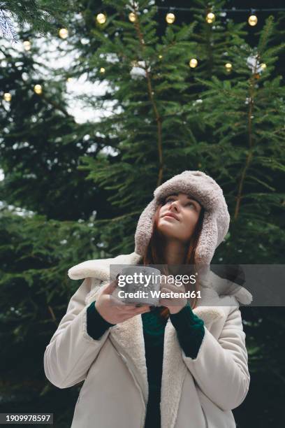 young woman in hunters cap holding coffee cup in hand - jägermütze stock-fotos und bilder