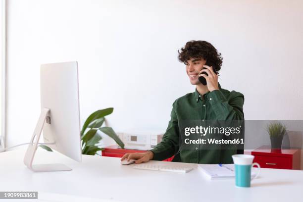smiling businessman doing multi-tasking at home office - grünes hemd stock-fotos und bilder