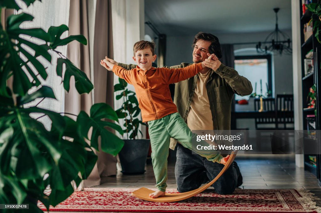 Smiling father helping son to balance on board at home