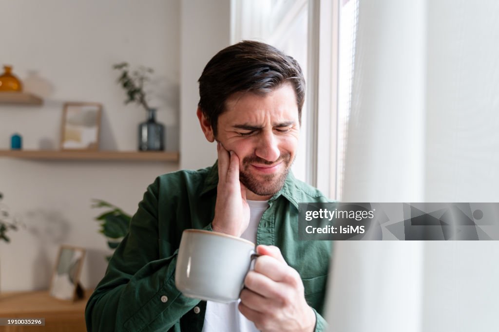 Pensive man holding cheek, suffering from dental pain.
