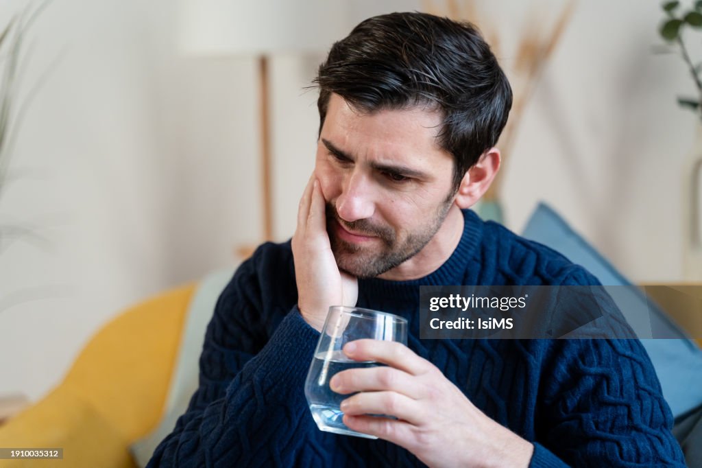 Pensive man holding cheek, suffering from dental pain.