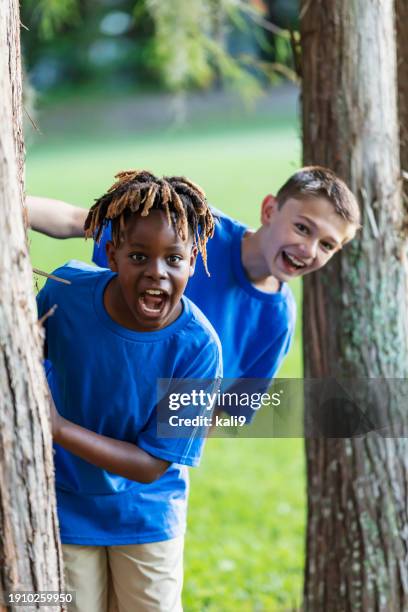 two boys playing at park, peeking out from behind trees - only boys stock pictures, royalty-free photos & images