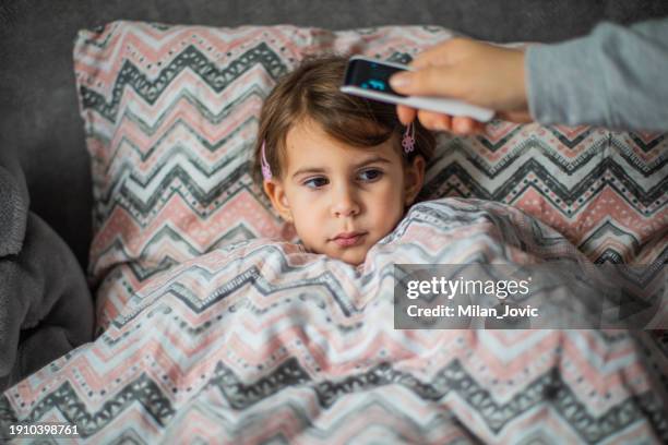 caring mother measuring her daughter temperature with digital thermometer - infrared thermometer stock pictures, royalty-free photos & images