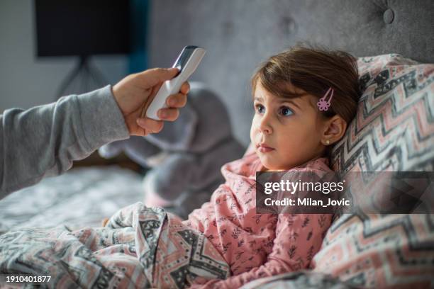 caring mother measuring her daughter temperature with digital thermometer - infrared thermometer stock pictures, royalty-free photos & images