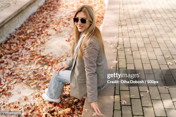 portrait of smiling young woman sitting on footpath - peel park stock pictures, royalty-free photos & images