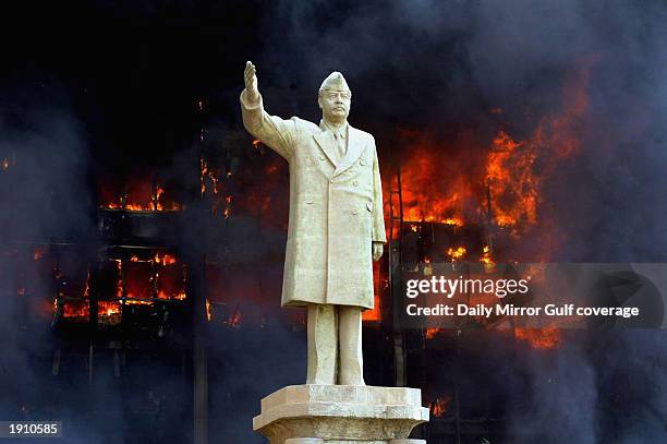 Statue of Saddam Hussein stands in front of the burning offices of his son Uday, April 9, 2003.