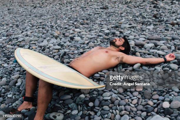 surfer relaxing on pebble beach after surfing - lying stock pictures, royalty-free photos & images