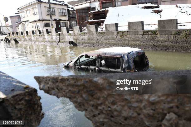 Vehicle believed to be washed away by the tsunami sits in water next to damaged buildings in the disaster-hit city of Noto, Ishikawa prefecture on...