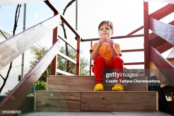 a boy eats ice cream while sitting on the steps of his house. - rim light portrait stock pictures, royalty-free photos & images