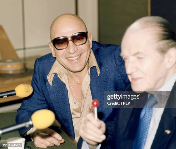 Greek American actor Telly Savalas and an unidentified man pose for a portrait during a press conference in London, England, November 10, 1975.