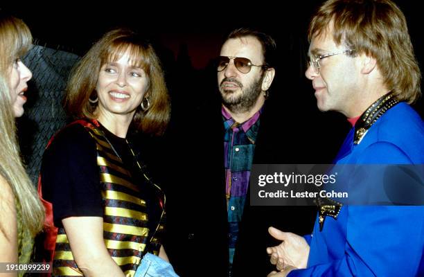 American actress Barbara Bach, English musicians Ringo Starr and Elton John talk to an unidentified woman in Los Angeles, California, circa 1990.