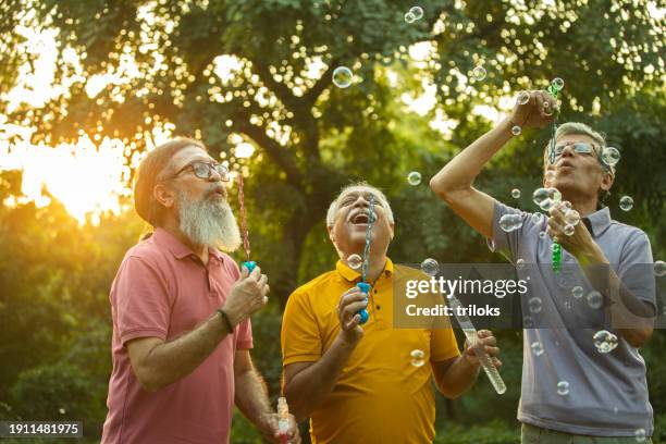 carefree old male friends blowing bubbles in park - bubble stock pictures, royalty-free photos & images