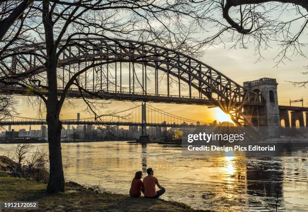 Couple Enjoying Sunset Near Hell Gate And Rfk Triboro Bridges, Ralph Demarco Park. Queens, New York, United States Of America.